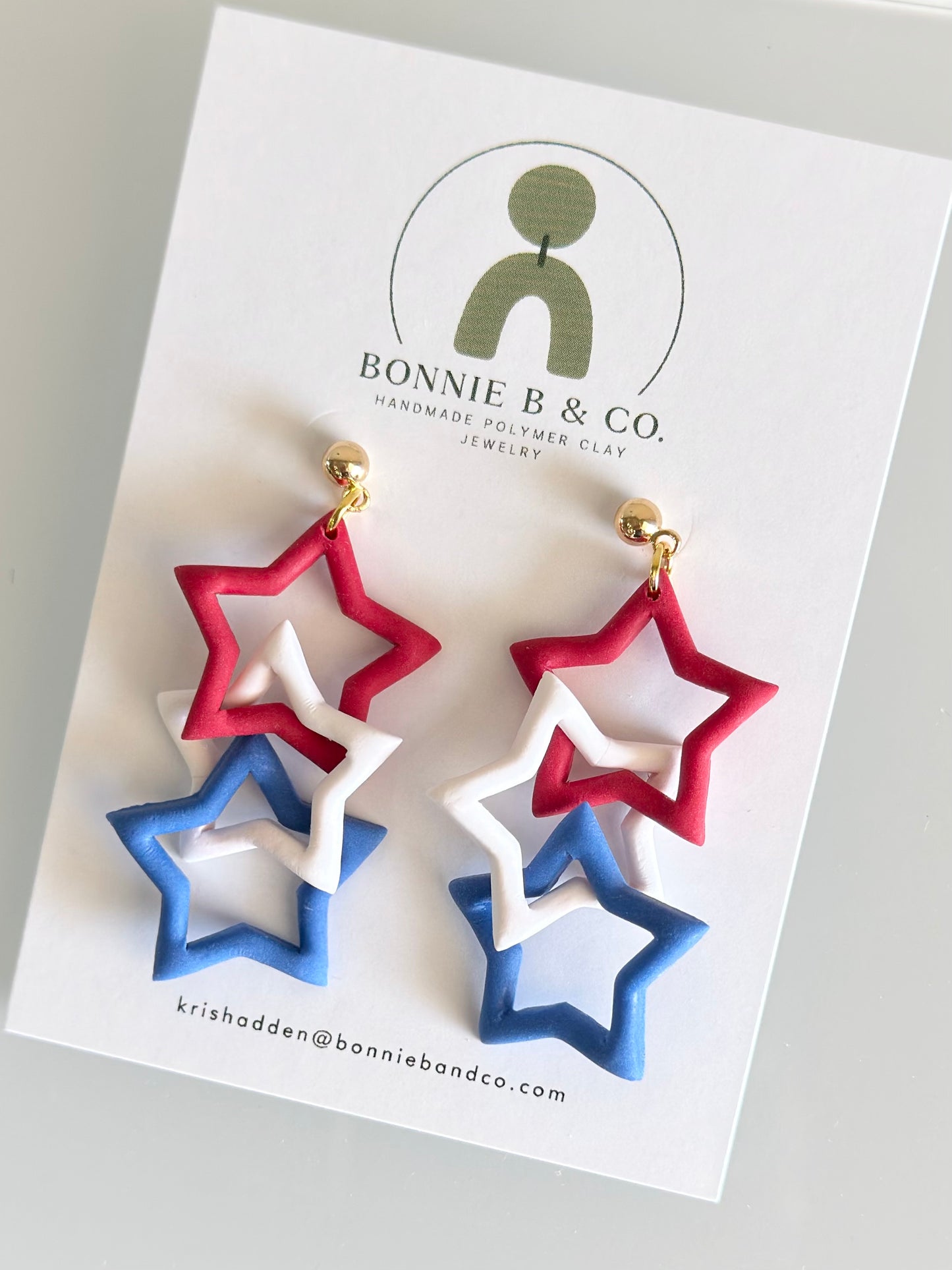 Red white and blue patriotic star polymer clay dangle earrings with gold hardware on Bonnie B & Co display card