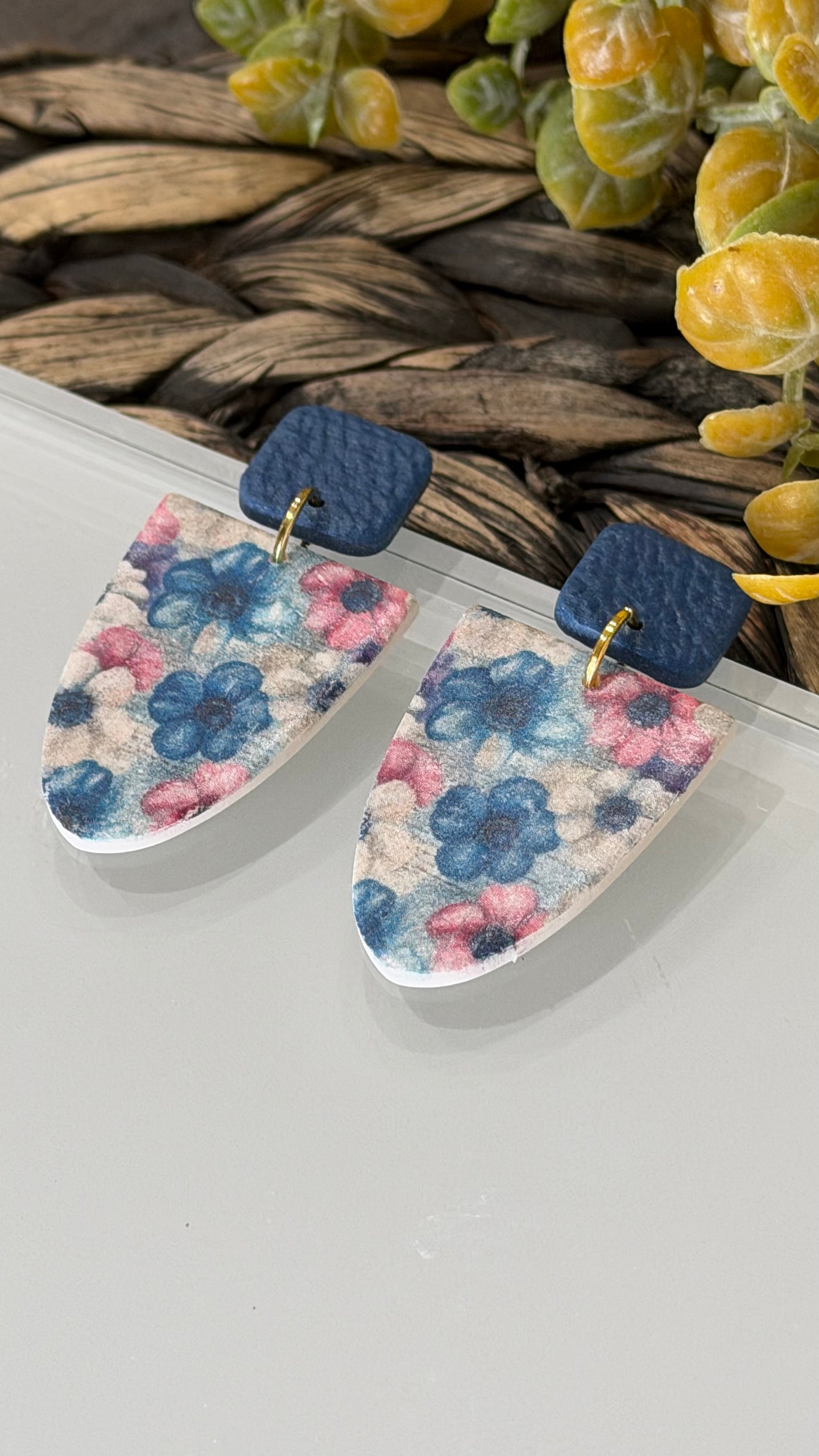 Handmade polymer clay dangle earrings with navy blue textured studs and soft blue and pink floral pattern on white clay