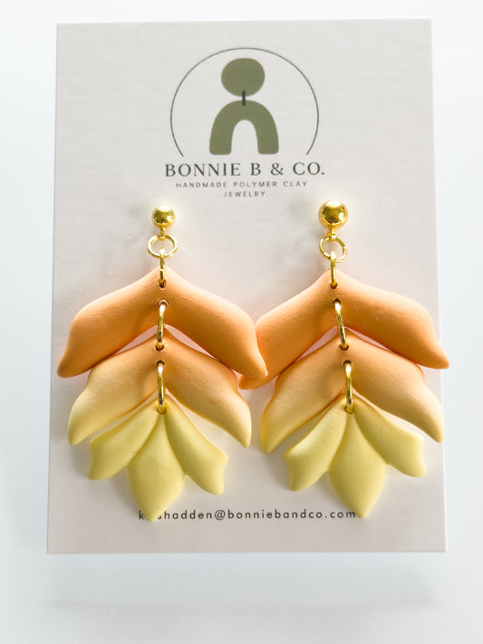 Handmade polymer clay dangle earrings in a warm sunset gradient, featuring layered terracotta and soft yellow tones in a boho style