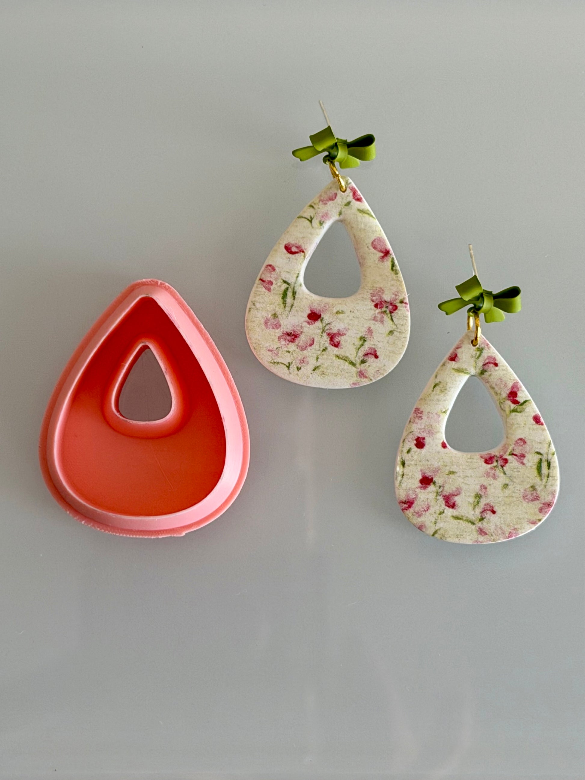 Modern open teardrop polymer clay cutter beside floral earrings made with the cutter.
