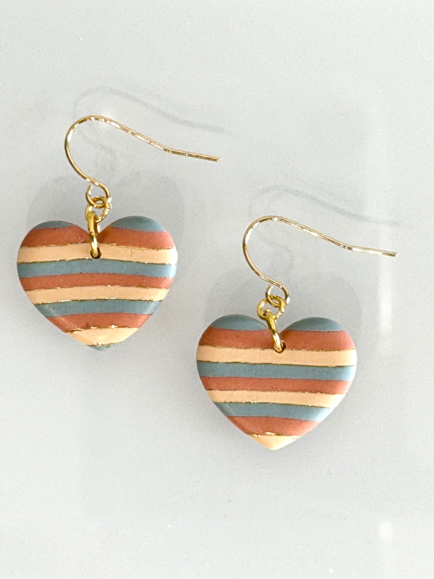 Handmade boho heart earrings in desert tones displayed with gold hooks and striped clay design