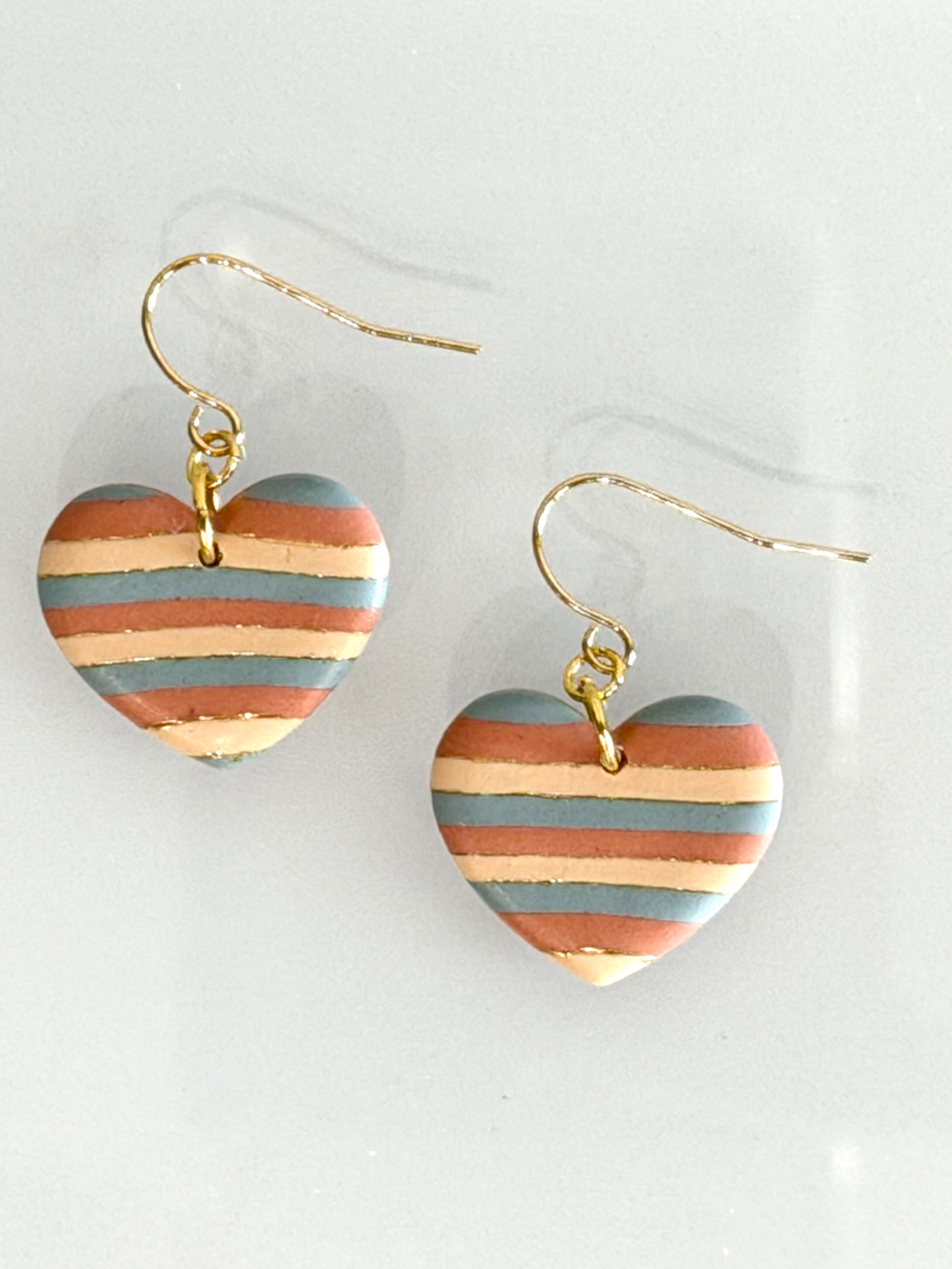 Handmade boho heart earrings in desert tones displayed with gold hooks and striped clay design