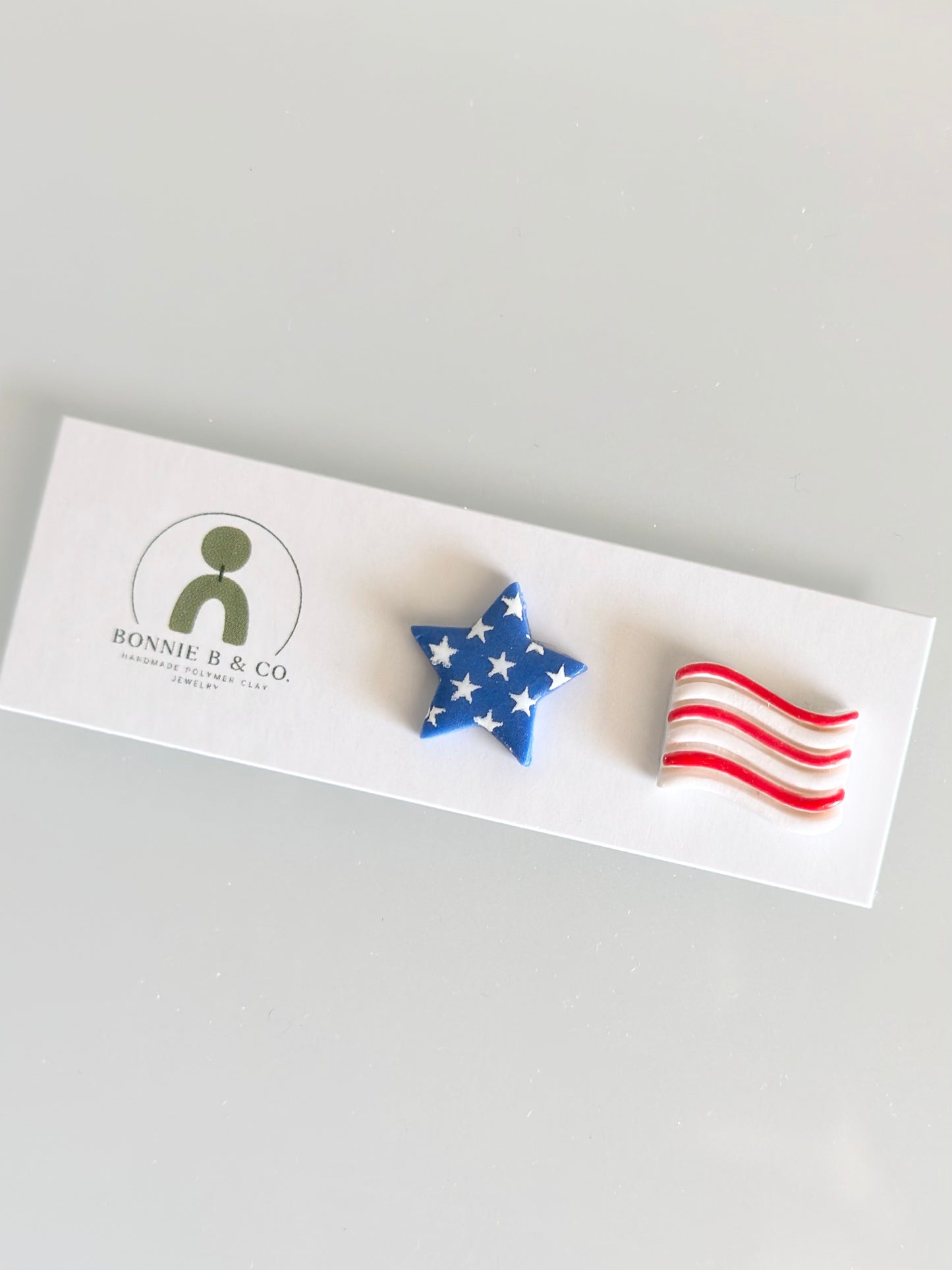 Handmade patriotic polymer clay stud earrings featuring a blue star with white stars and a red, white, and blue American flag design.