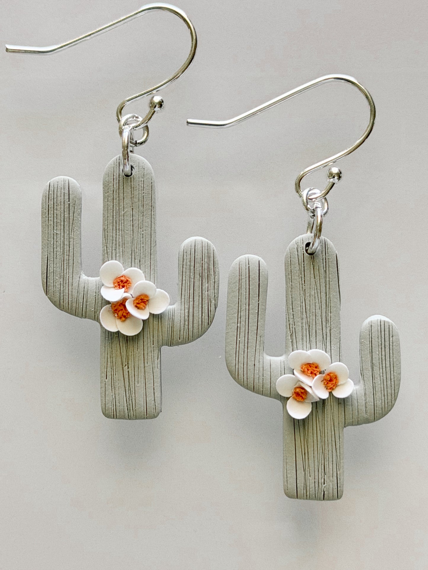 Handmade polymer clay saguaro cactus earrings with white blossom flowers and textured sage green finish