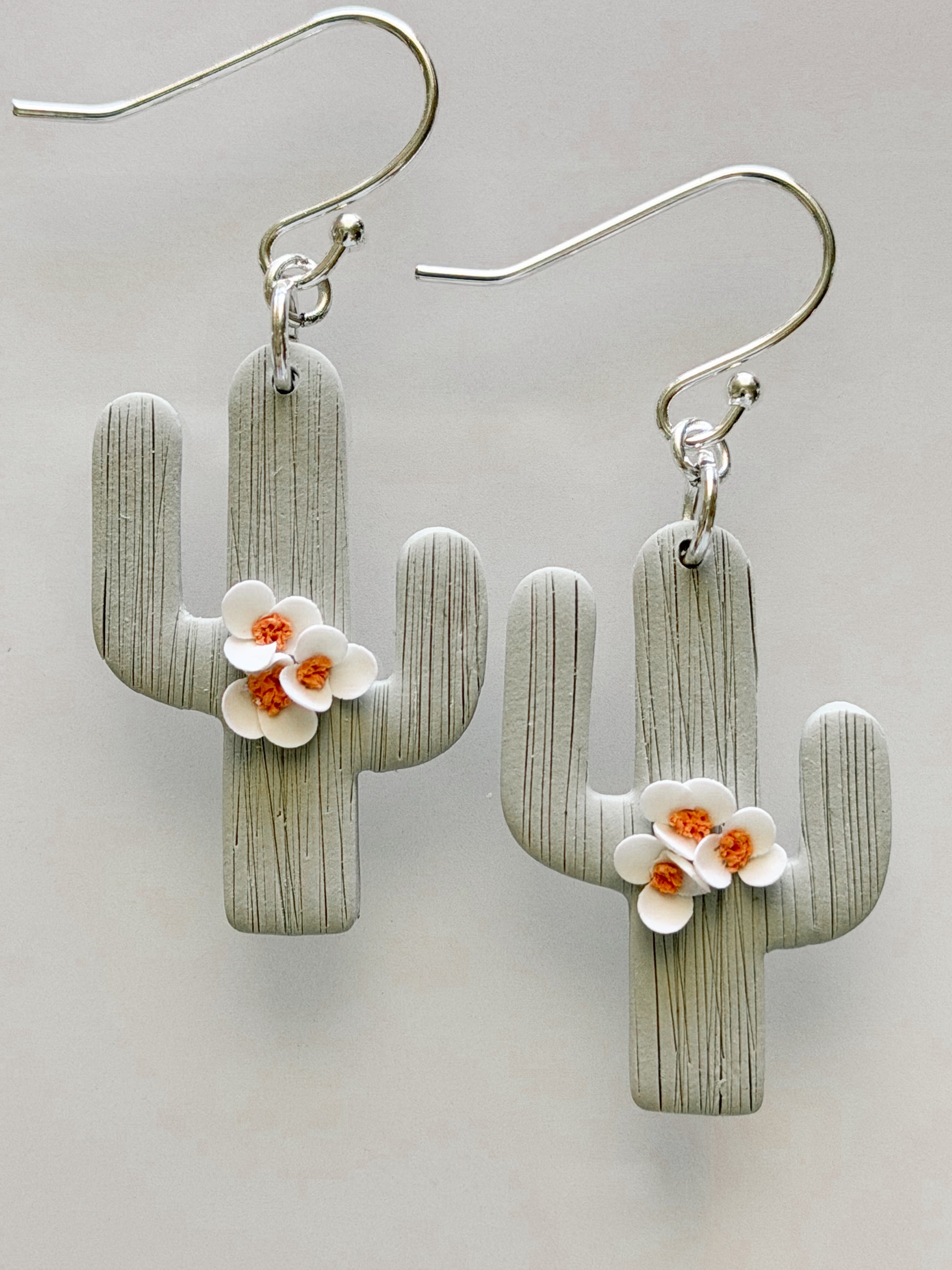 Handmade polymer clay saguaro cactus earrings with white blossom flowers and textured sage green finish